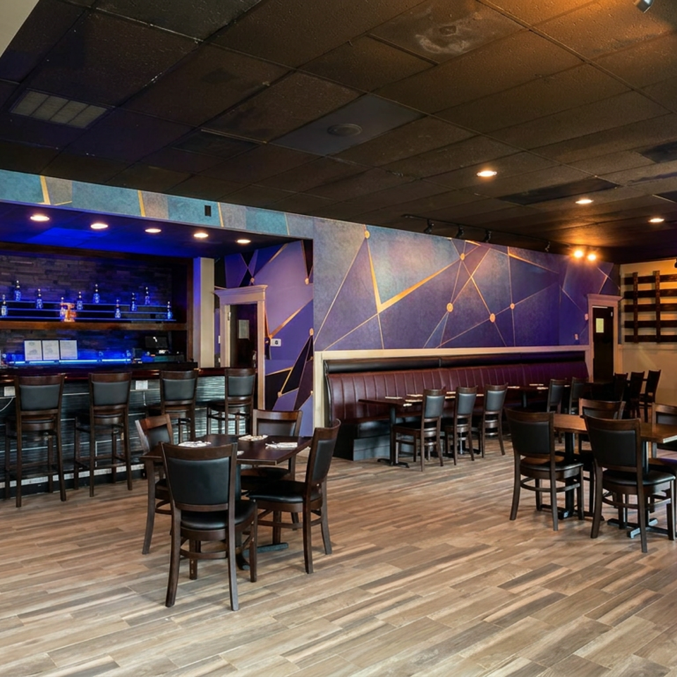 Modern restaurant interior with blue geometric walls, bar seating, dining tables, and illuminated LAZEEZ sign.